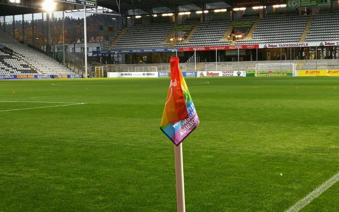Eine Eckfahne in einem Stadion. Die Eckfahne ist in Regenbogenfarben